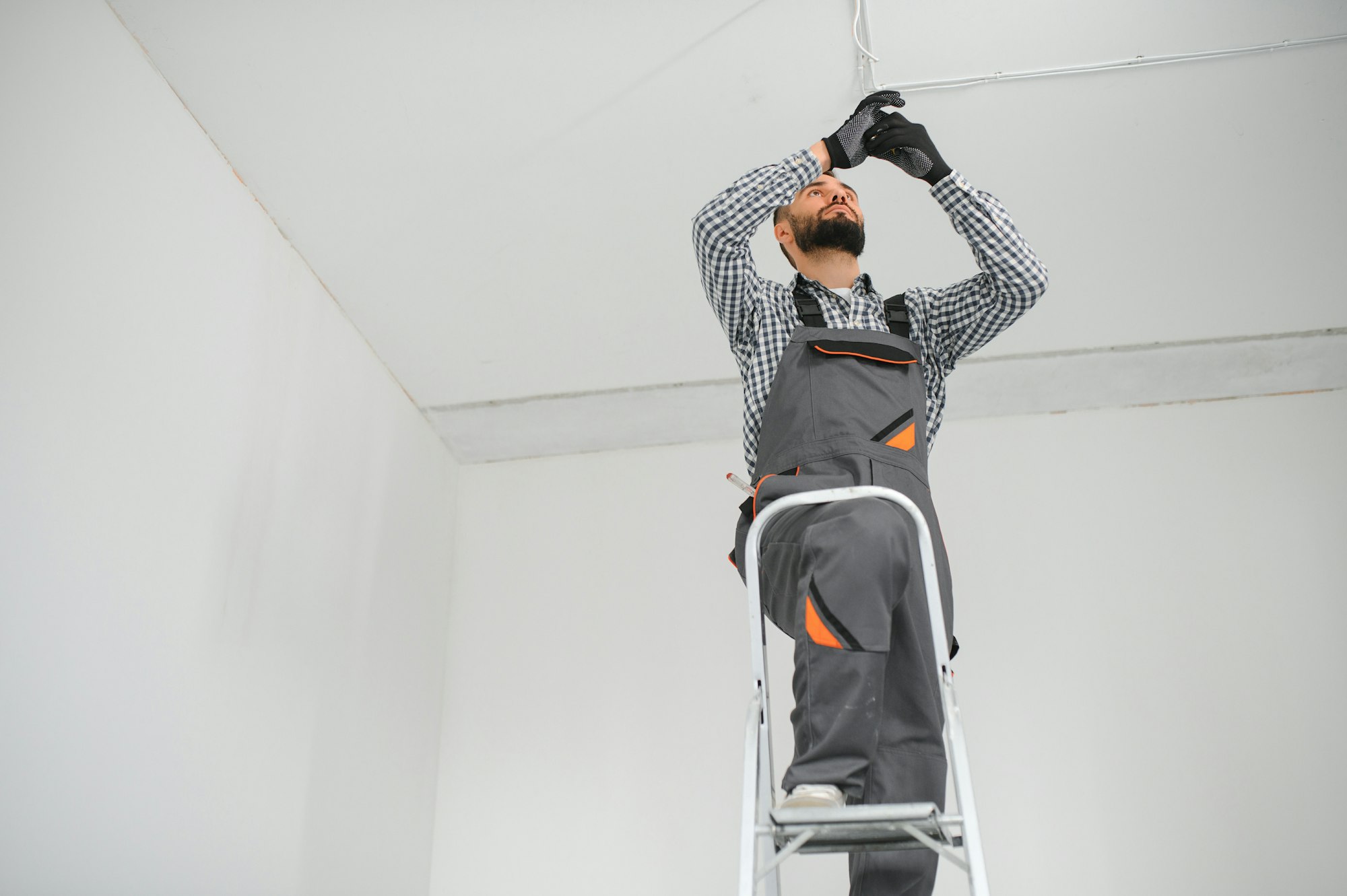 Young electrician installing smoke detector on ceiling.